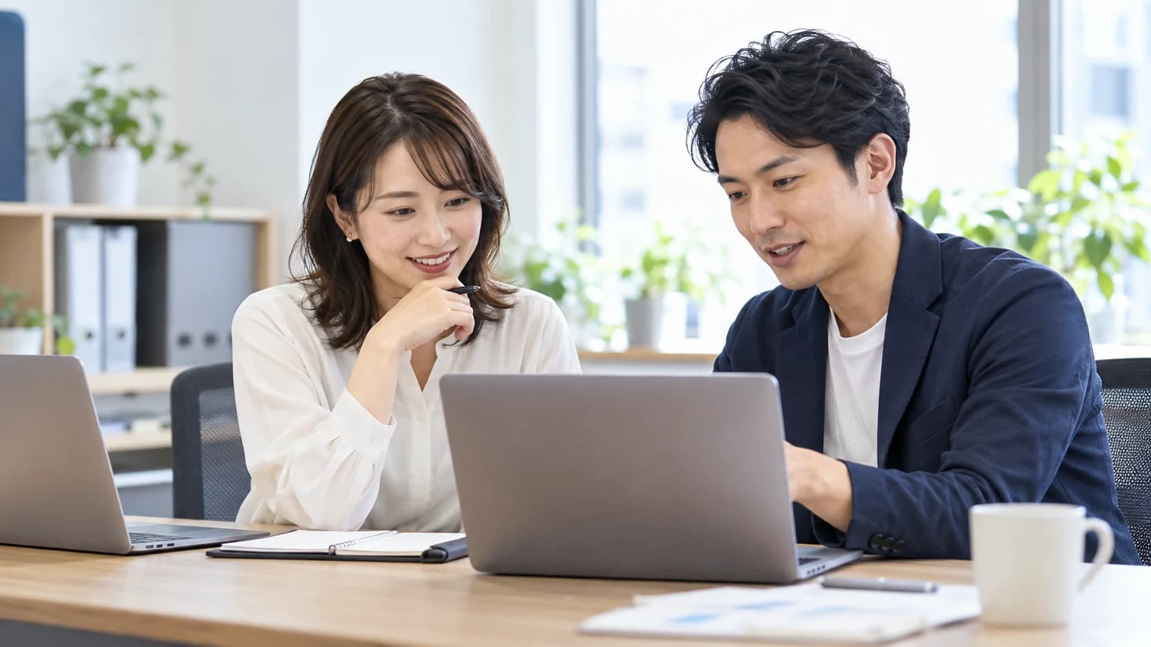 2人の社員がノートパソコンで資料を確認しながら共同作業を進めるイメージ